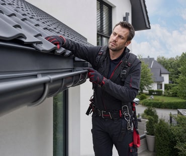 Dachdecker reinigt und kontrolliert eine Zinkdachrinne