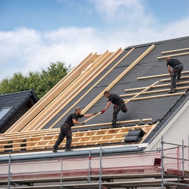 Handwerker verlegen Dämmung zwischen den Sparren eines Dachstuhls